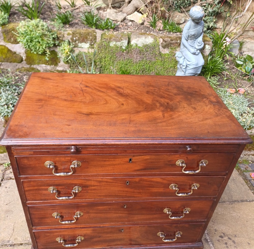 A small Georgian mahogany chest of drawers featuring four graduated drawers, brass swan-neck handles, a pull-out brushing slide, and bracket feet. View VI