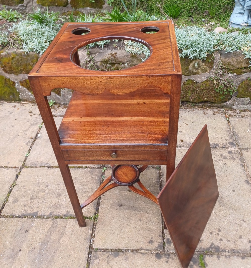 An antique Georgian mahogany bedside table featuring an open top tier with a scalloped apron, a single drawer with a brass pull, square legs, and an X-shaped stretcher with a central circular platform. View VII