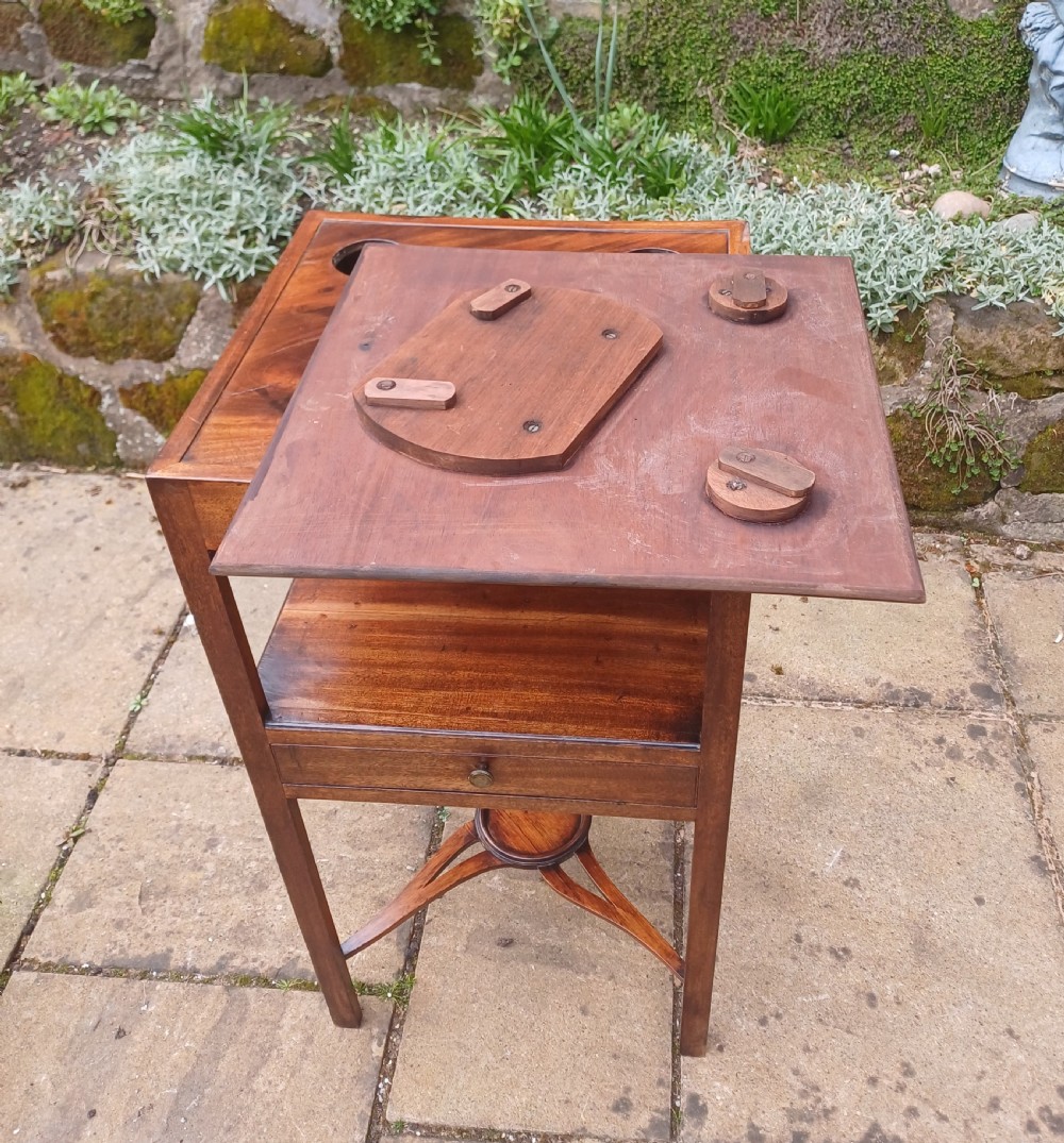 An antique Georgian mahogany bedside table featuring an open top tier with a scalloped apron, a single drawer with a brass pull, square legs, and an X-shaped stretcher with a central circular platform. View VIII