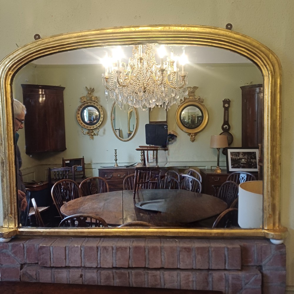 A Victorian giltwood overmantel mirror featuring an arched top frame and moulded gold finish.