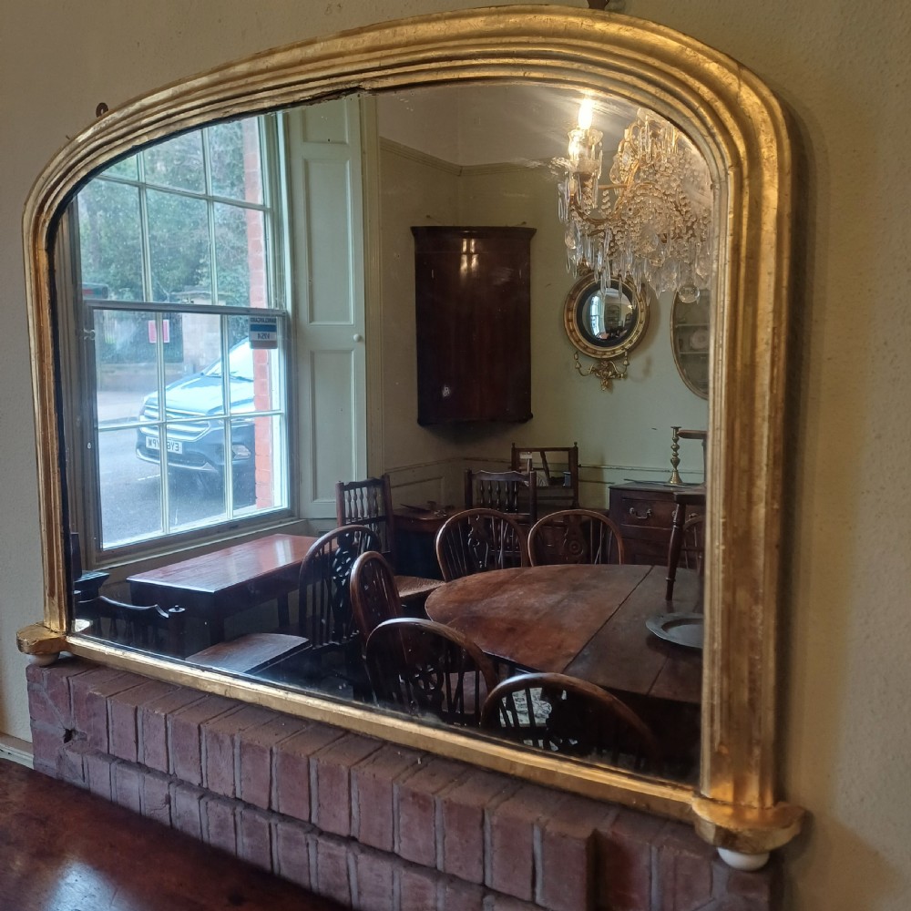 A Victorian giltwood overmantel mirror featuring an arched top frame and moulded gold finish. View VI