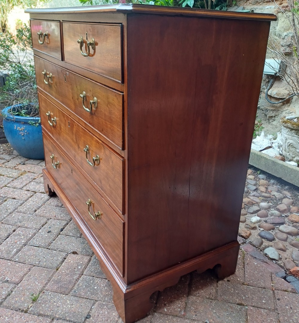 A Georgian mahogany chest of drawers featuring a two-over-three drawer configuration, brass swan-neck handles, keyholes, and bracket feet. View V