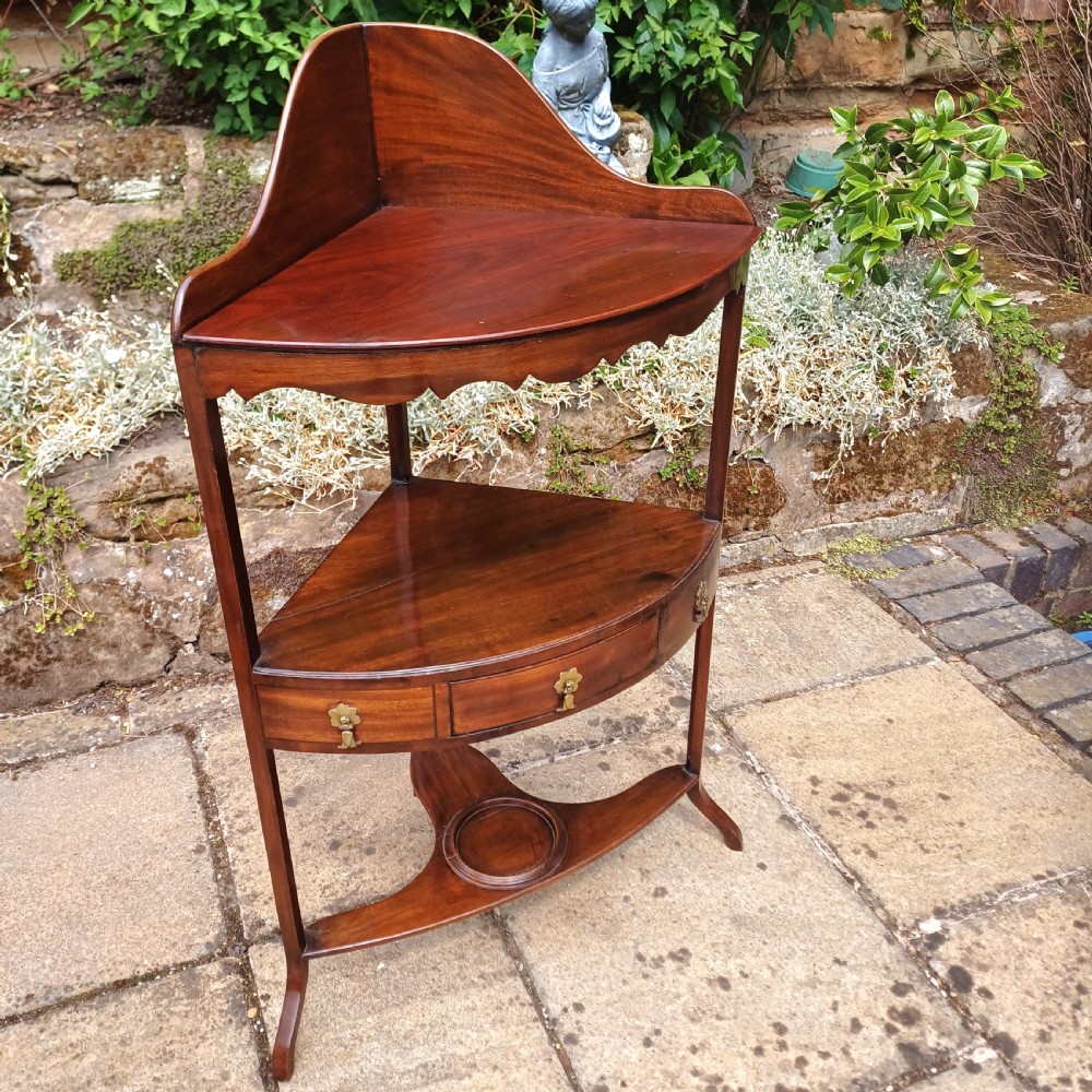 A Georgian mahogany corner washstand featuring a curved splashback, middle drawer with brass handles, and lower stretcher with a basin ring. View II