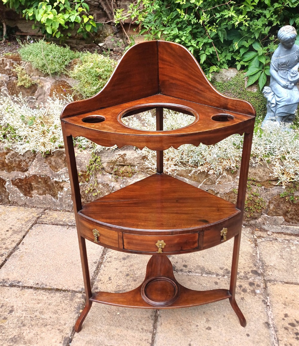 A Georgian mahogany corner washstand featuring a curved splashback, middle drawer with brass handles, and lower stretcher with a basin ring. View III