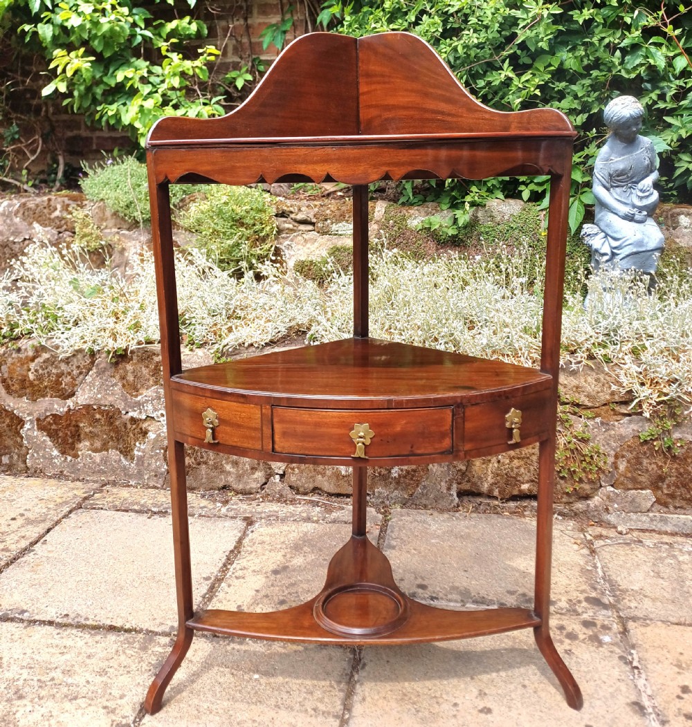 A Georgian mahogany corner washstand featuring a curved splashback, middle drawer with brass handles, and lower stretcher with a basin ring. View V