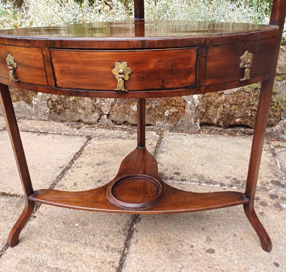 A Georgian mahogany corner washstand featuring a curved splashback, middle drawer with brass handles, and lower stretcher with a basin ring. View X