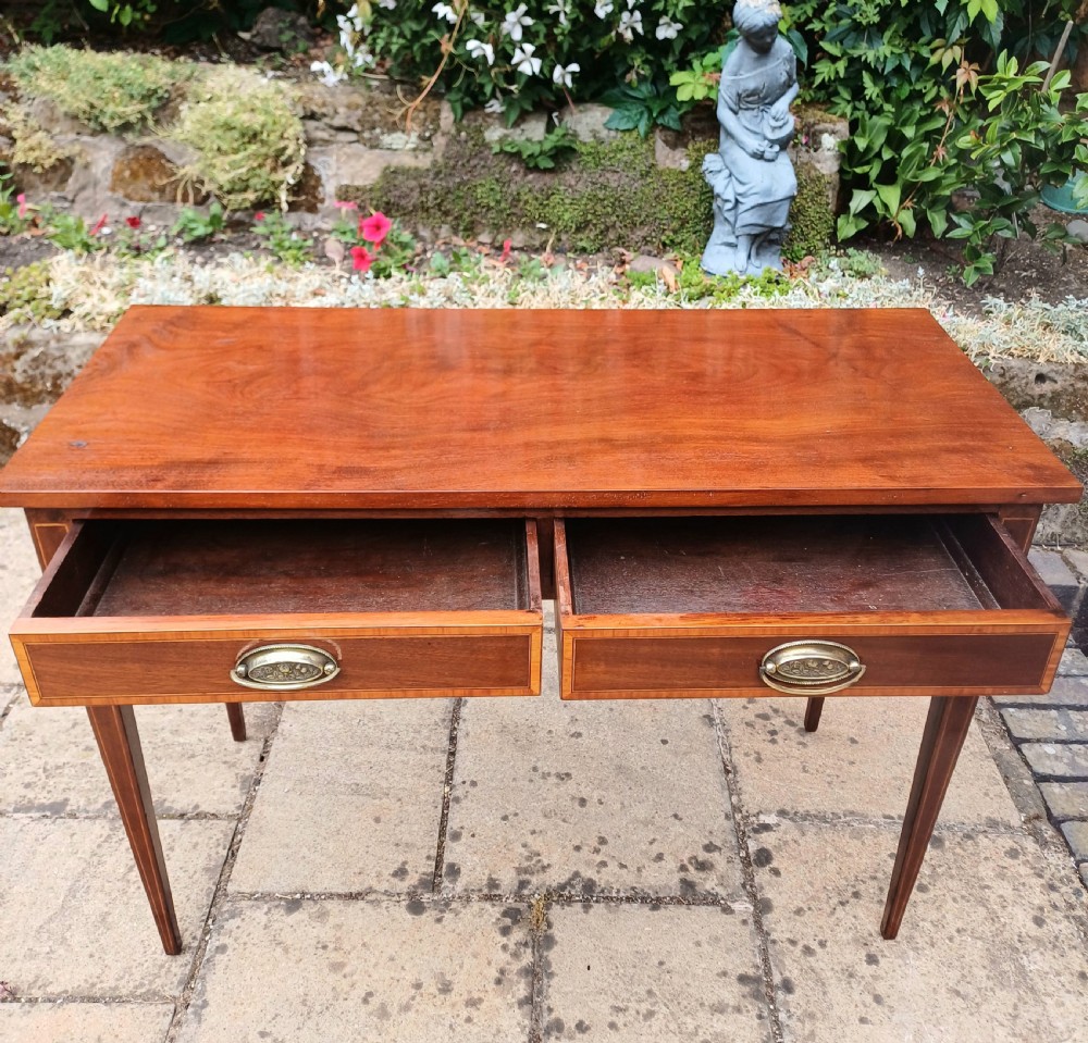 An Edwardian mahogany writing table featuring two inlaid drawers, brass oval drop handles, and slender tapered legs. View III