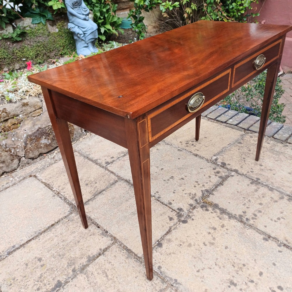 An Edwardian mahogany writing table featuring two inlaid drawers, brass oval drop handles, and slender tapered legs. View V