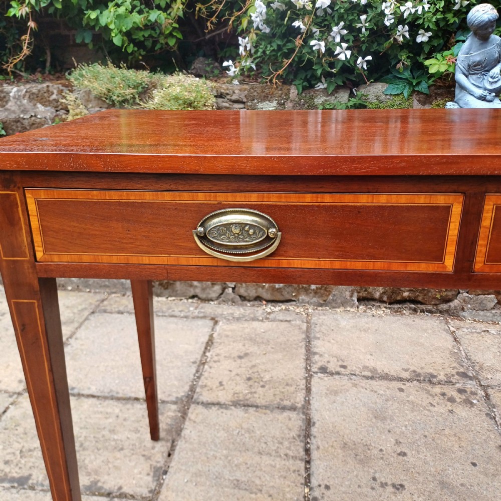 An Edwardian mahogany writing table featuring two inlaid drawers, brass oval drop handles, and slender tapered legs. View VI