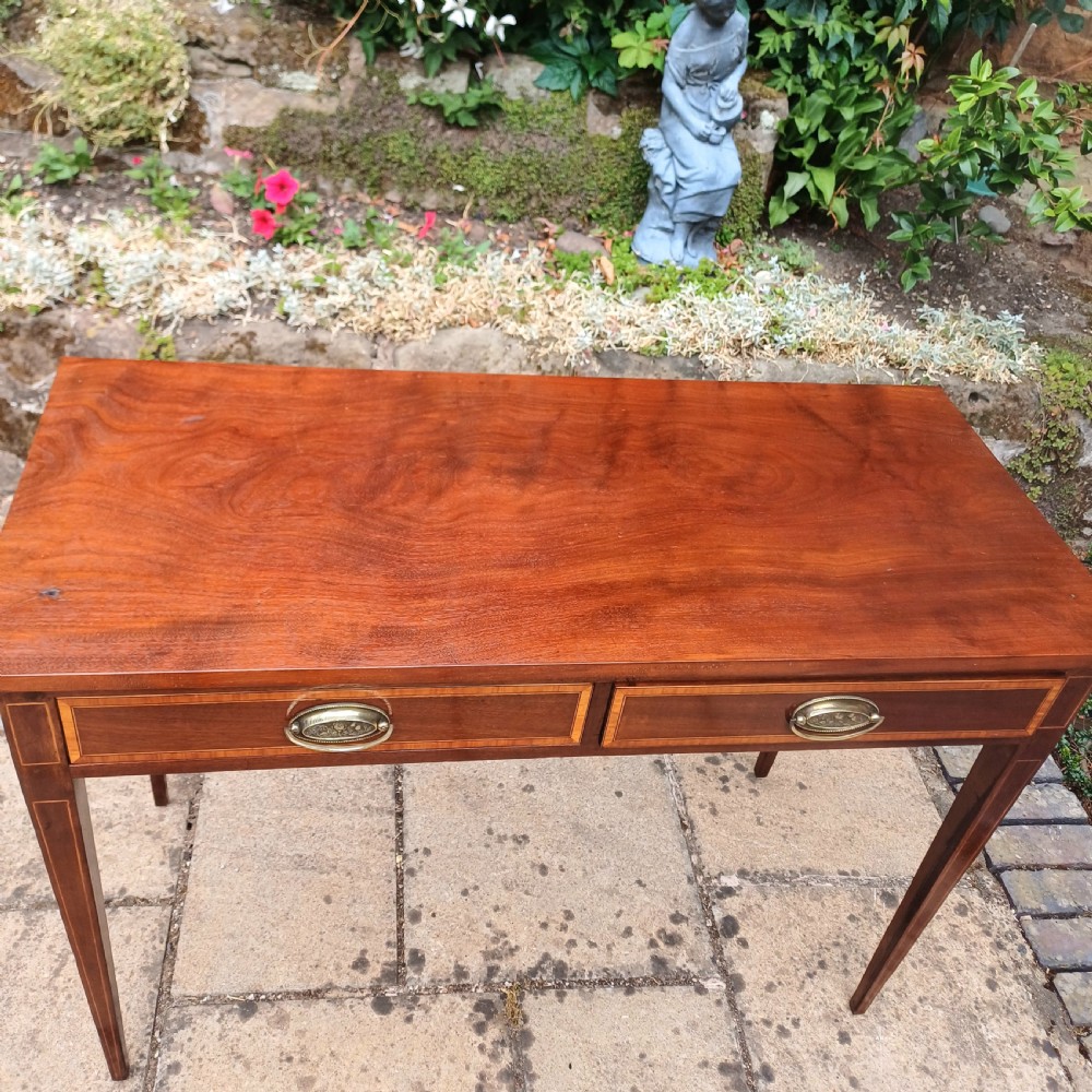An Edwardian mahogany writing table featuring two inlaid drawers, brass oval drop handles, and slender tapered legs. View VII