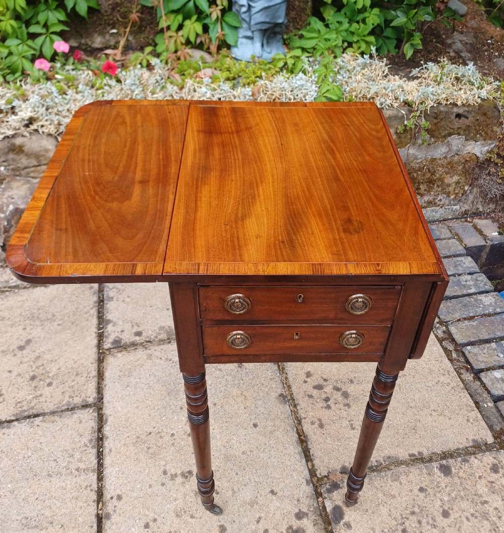 A Regency mahogany miniature Pembroke table featuring two drop leaves, two drawers with brass ring handles, and turned reeded legs on castors. View VI