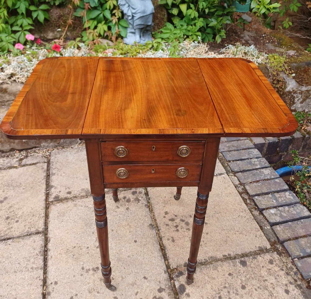 A Regency mahogany miniature Pembroke table featuring two drop leaves, two drawers with brass ring handles, and turned reeded legs on castors. View VII