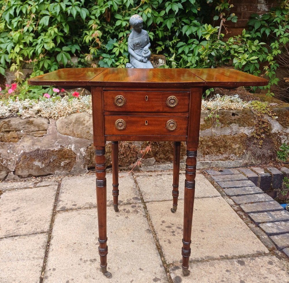 A Regency mahogany miniature Pembroke table featuring two drop leaves, two drawers with brass ring handles, and turned reeded legs on castors. View VIII