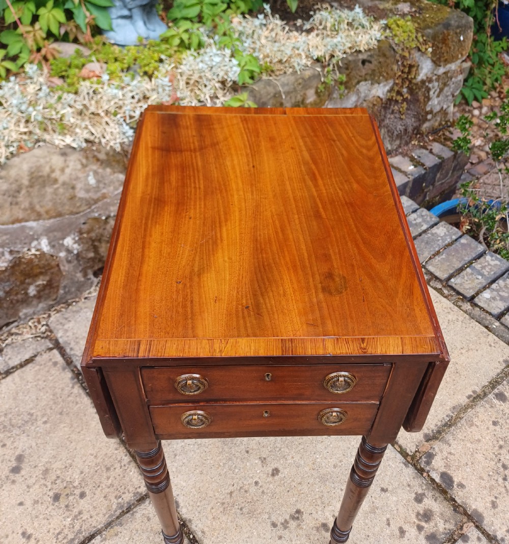 A Regency mahogany miniature Pembroke table featuring two drop leaves, two drawers with brass ring handles, and turned reeded legs on castors. View XI