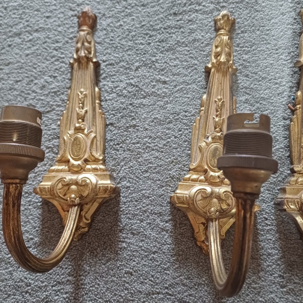 A set of four ornate gilded brass single-arm wall sconces featuring tapered backplates with classical scroll detailing. View III