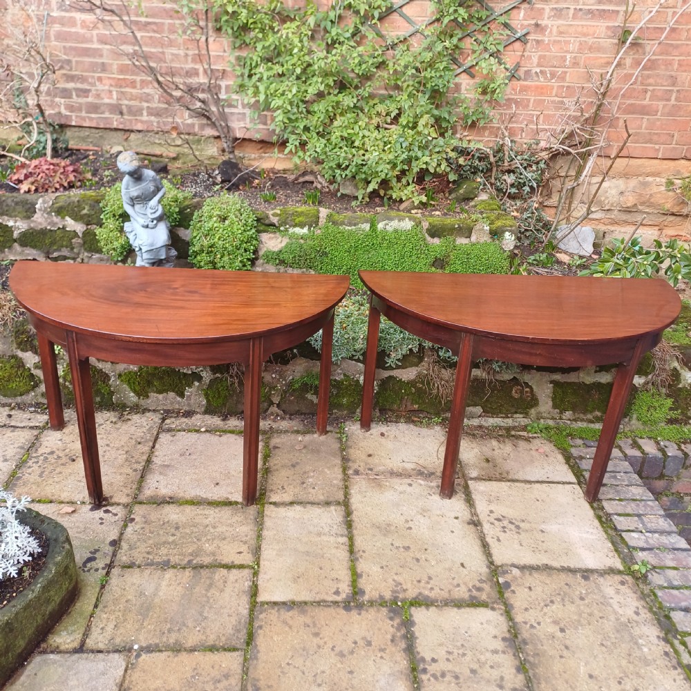 A pair of Georgian mahogany demi-lune tables with semi-circular tops and straight tapered legs.