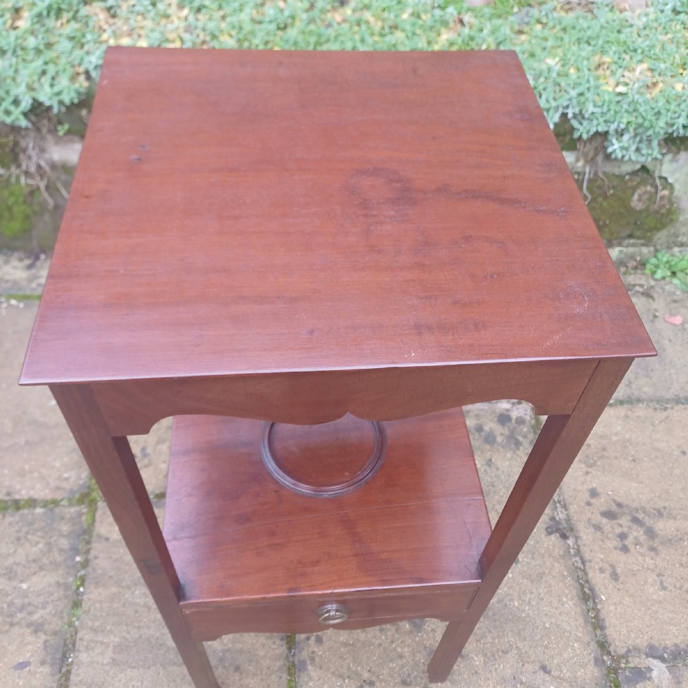 A two-tier Georgian mahogany bedside table featuring a square top, a lower shelf with a circular inset recess, a single drawer with a brass ring handle, and scalloped aprons. View V