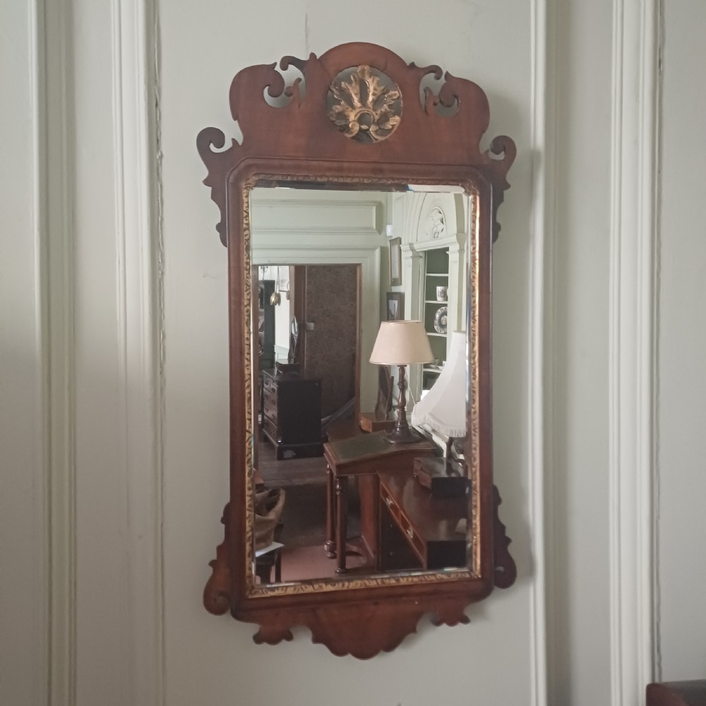 An antique Georgian mahogany wall mirror featuring a scrollwork fretwork frame, a gilded inner slip, and a round carved gilt emblem at the cresting.