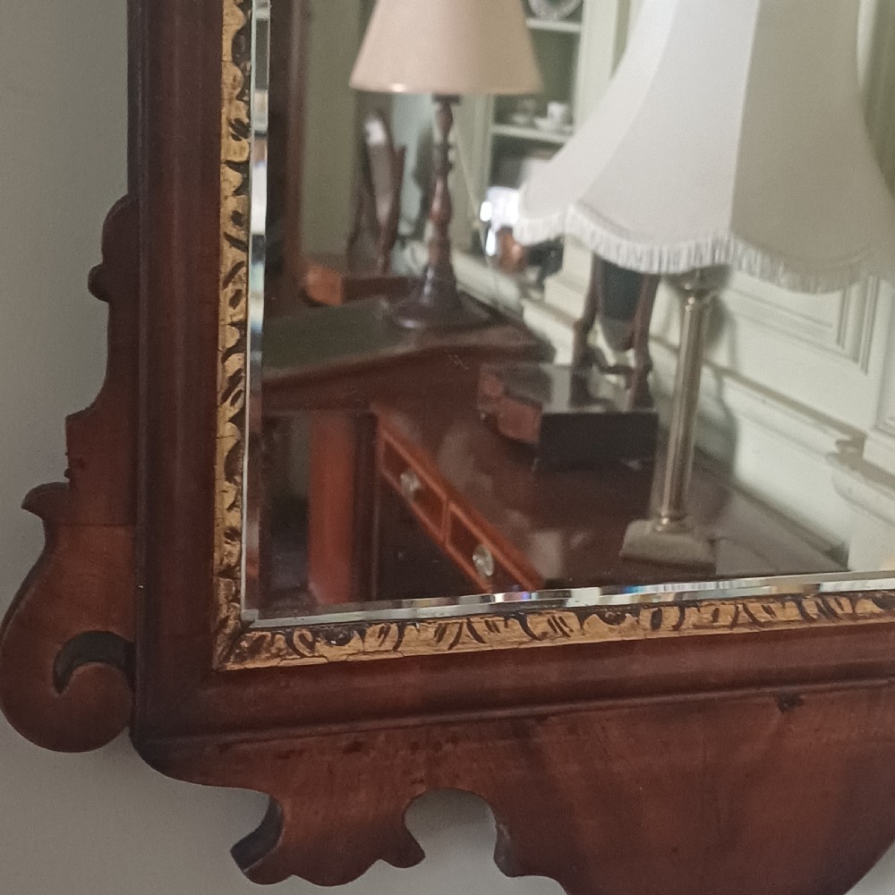 An antique Georgian mahogany wall mirror featuring a scrollwork fretwork frame, a gilded inner slip, and a round carved gilt emblem at the cresting. View IV