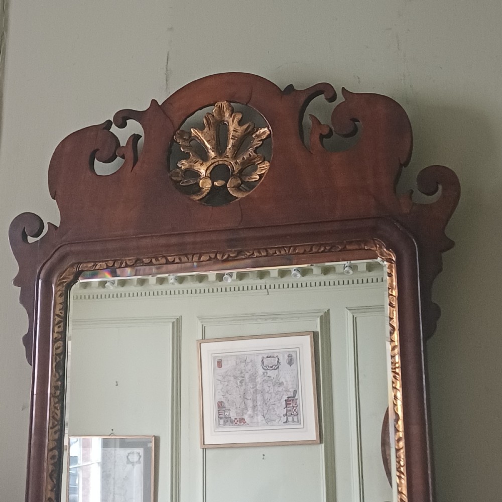 An antique Georgian mahogany wall mirror featuring a scrollwork fretwork frame, a gilded inner slip, and a round carved gilt emblem at the cresting. View V