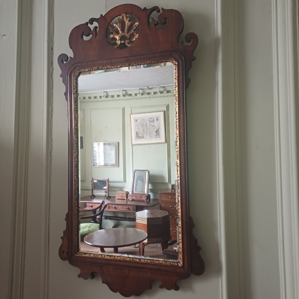 An antique Georgian mahogany wall mirror featuring a scrollwork fretwork frame, a gilded inner slip, and a round carved gilt emblem at the cresting. View VI
