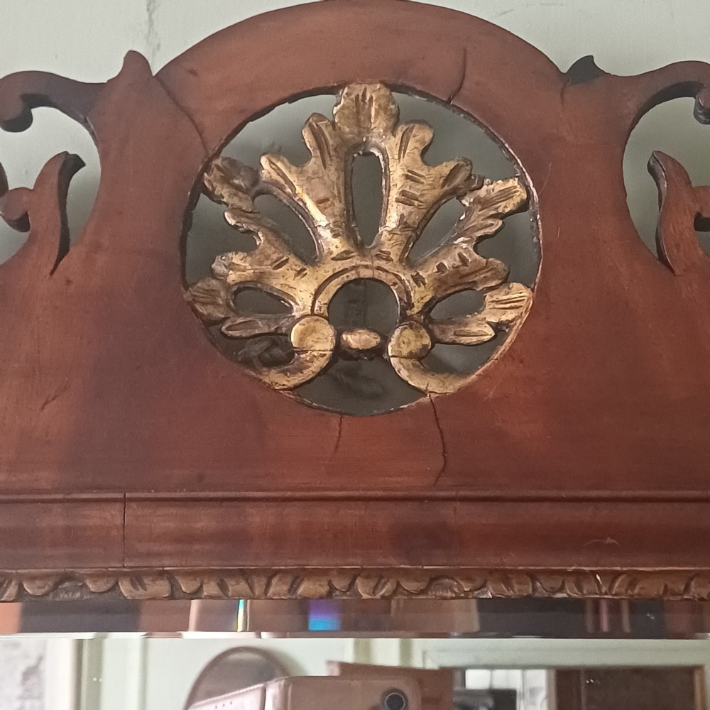 An antique Georgian mahogany wall mirror featuring a scrollwork fretwork frame, a gilded inner slip, and a round carved gilt emblem at the cresting. View II