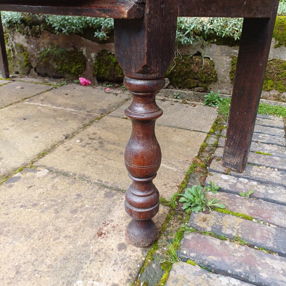 A late seventeenth-century dark oak dresser base featuring geometric mitred moulding across three drawers, turned front legs, and brass knob handles. View VII
