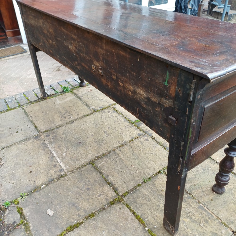 A late seventeenth-century dark oak dresser base featuring geometric mitred moulding across three drawers, turned front legs, and brass knob handles. View VIII