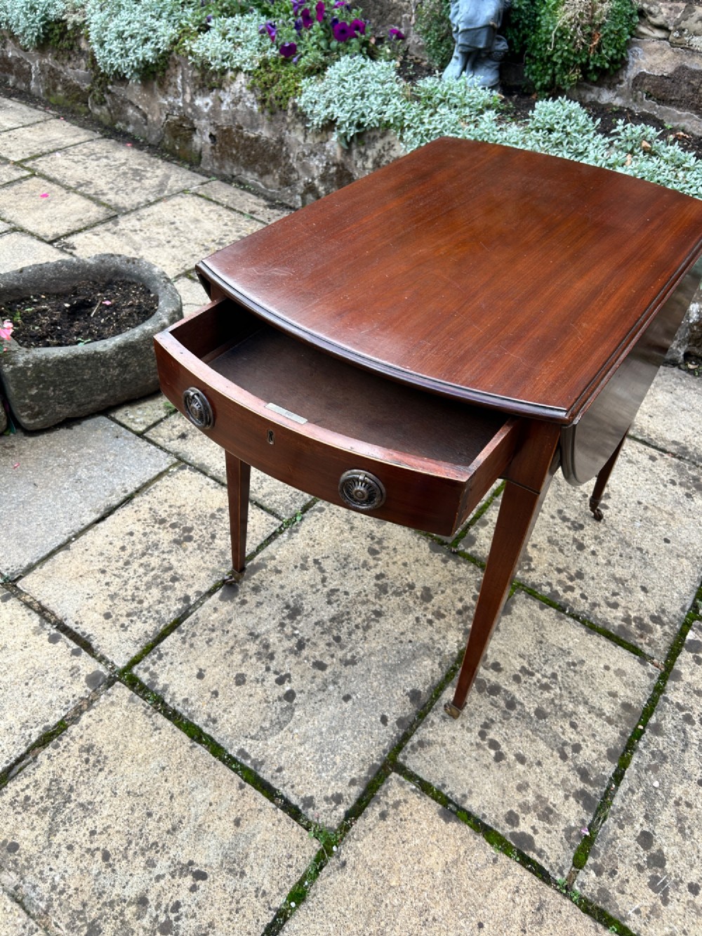An 18th-century oval mahogany Pembroke table featuring two drop leaves, a single drawer with brass ring handles, line inlay, and square tapered legs on castors. View II
