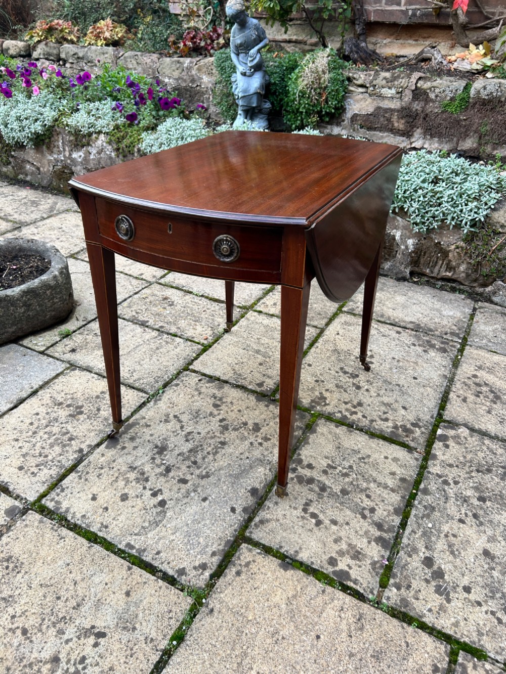 An 18th-century oval mahogany Pembroke table featuring two drop leaves, a single drawer with brass ring handles, line inlay, and square tapered legs on castors. View III