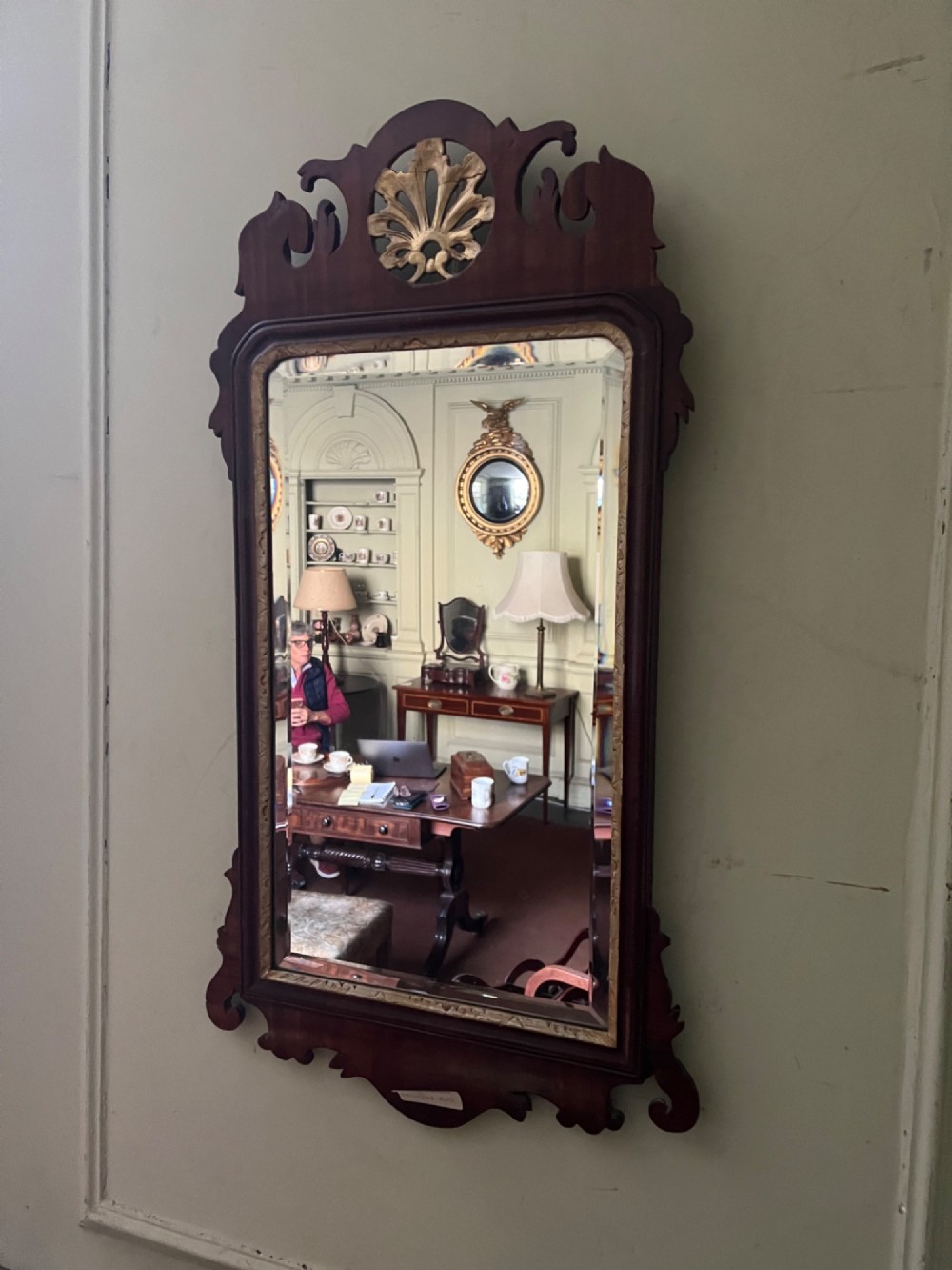 A vertical rectangular wall mirror with a dark mahogany frame, scroll-carved fretwork borders, and a gilded carved crest at the top.