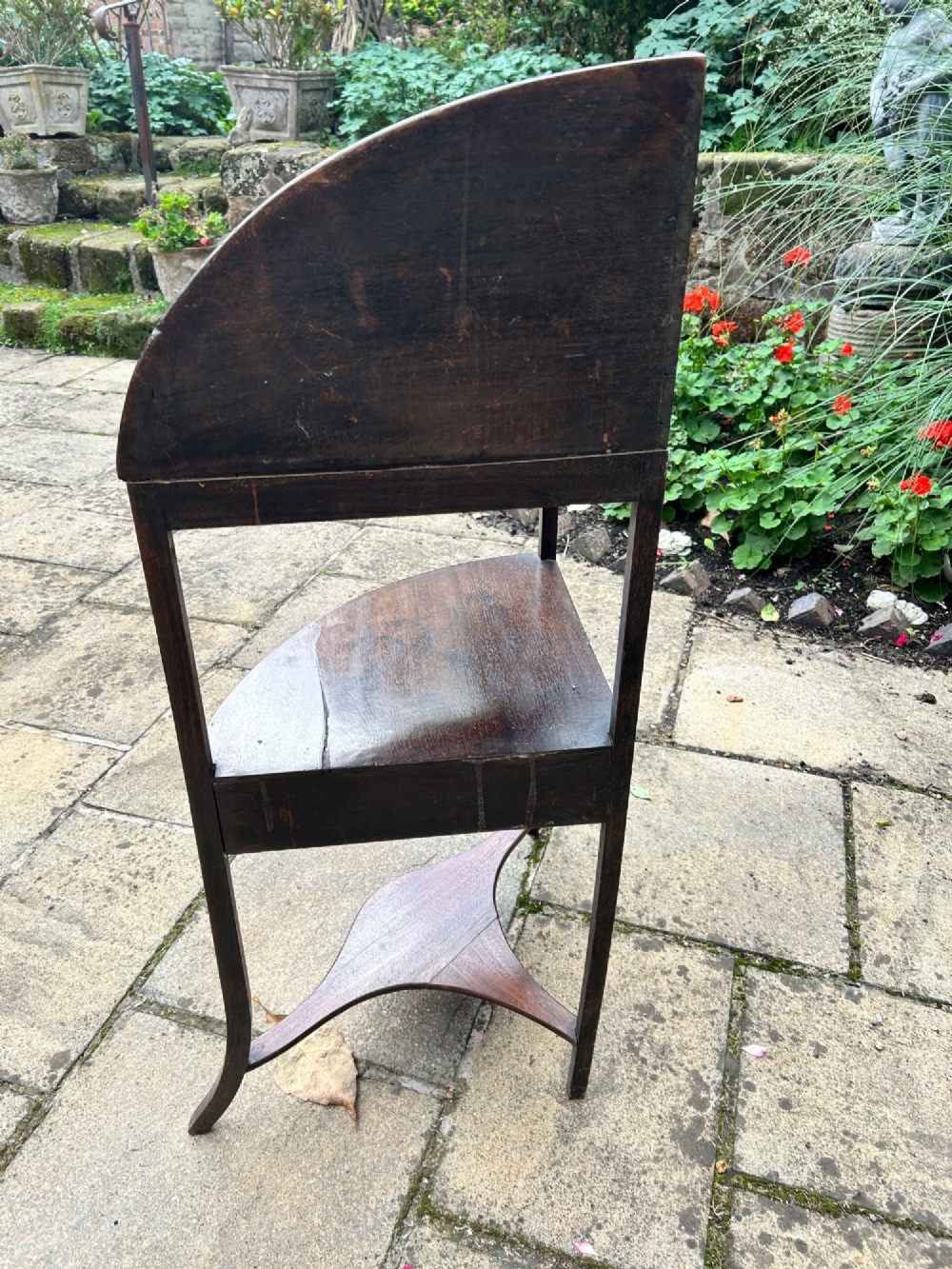 A late 18th-century mahogany corner washstand featuring a curved splashback with a small upper shelf, a middle drawer tier, and splayed legs connected by a shaped lower shelf. View III
