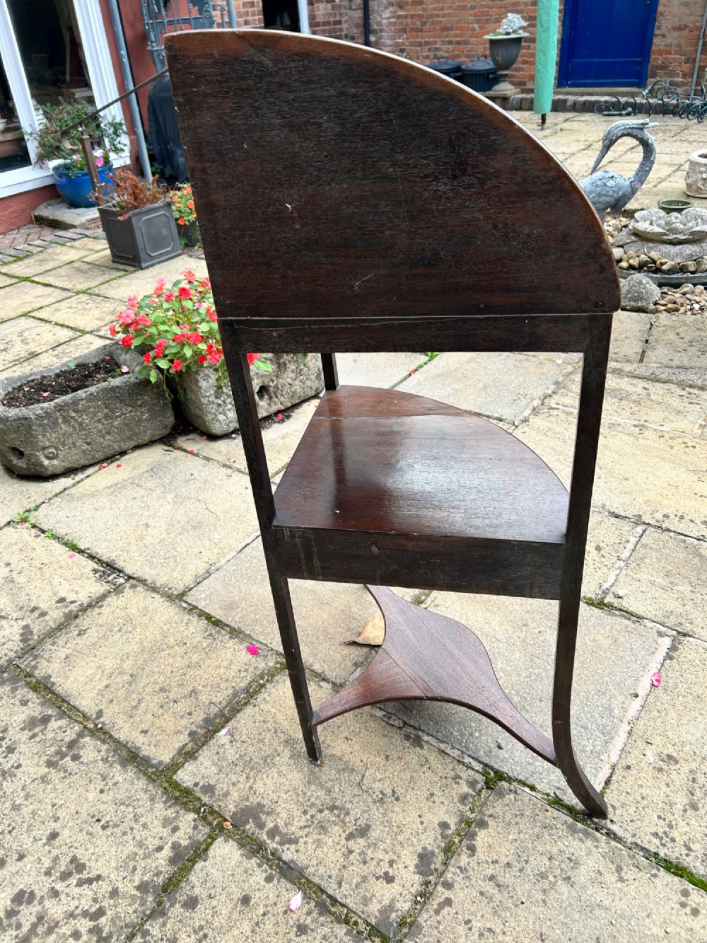 A late 18th-century mahogany corner washstand featuring a curved splashback with a small upper shelf, a middle drawer tier, and splayed legs connected by a shaped lower shelf. View IV