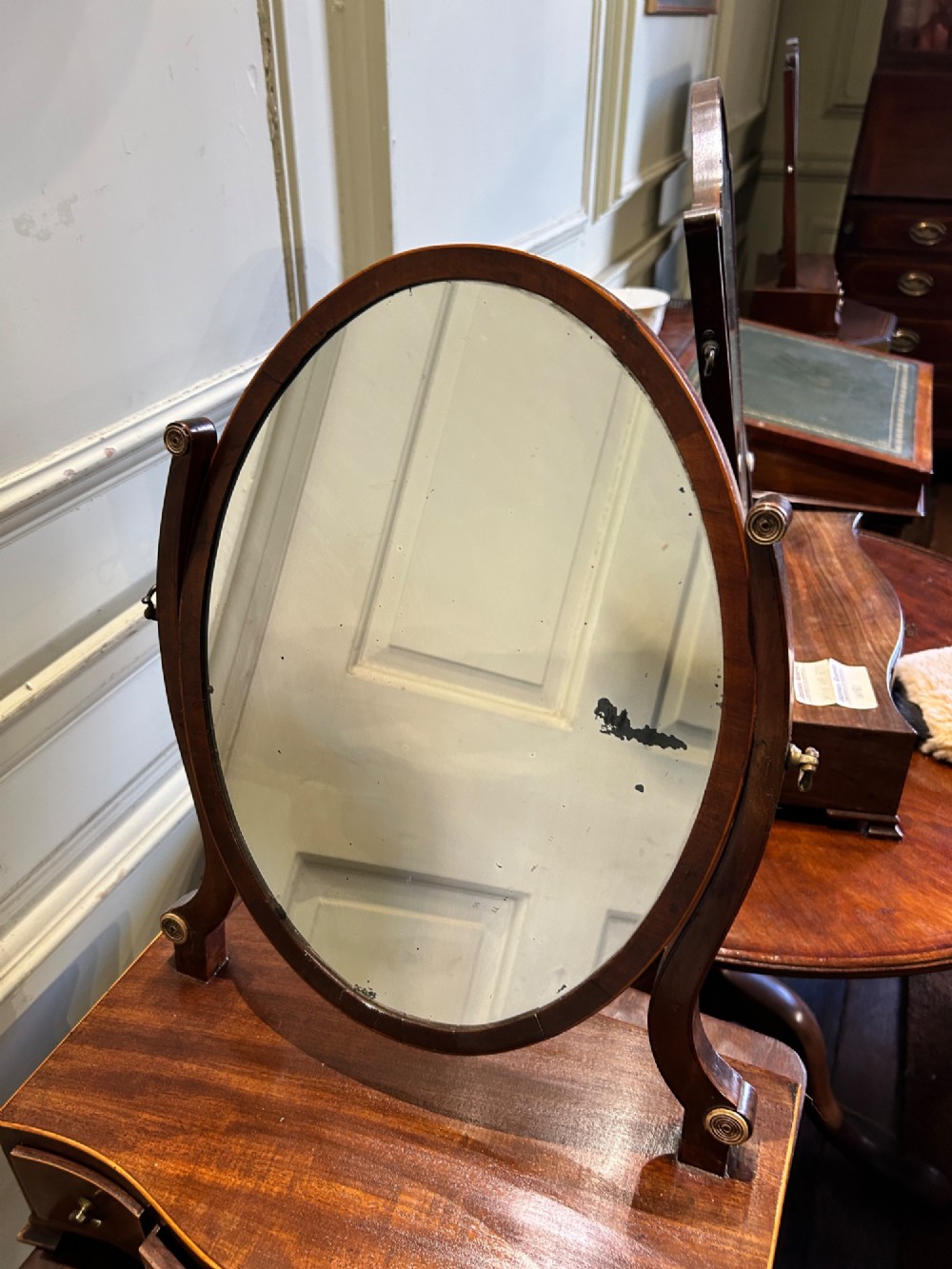A Georgian mahogany toilet mirror featuring an oval adjustable mirror supported by curved uprights, set upon a serpentine base with three small inlaid drawers and bracket feet. View IV