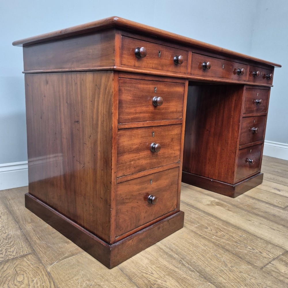 A 19th-century mahogany pedestal desk featuring nine drawers with turned wooden knobs and a solid plinth base.