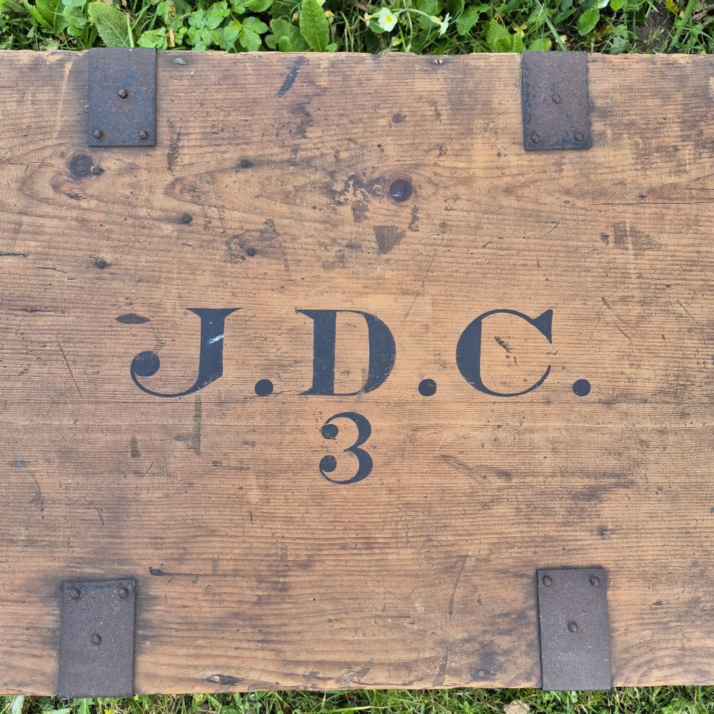 A pair of rectangular natural pine chests featuring black iron corner brackets, metal straps, keyhole escutcheons, and black stencilled text on the lids. View III