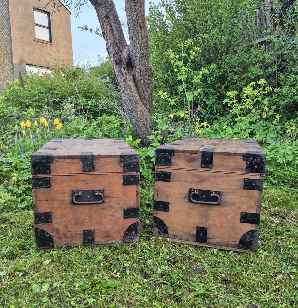 A pair of rectangular natural pine chests featuring black iron corner brackets, metal straps, keyhole escutcheons, and black stencilled text on the lids. View VII