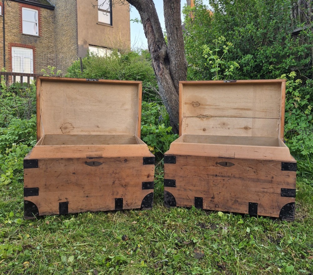 A pair of rectangular natural pine chests featuring black iron corner brackets, metal straps, keyhole escutcheons, and black stencilled text on the lids. View IX