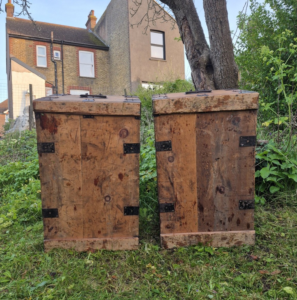 A pair of rectangular natural pine chests featuring black iron corner brackets, metal straps, keyhole escutcheons, and black stencilled text on the lids. View X