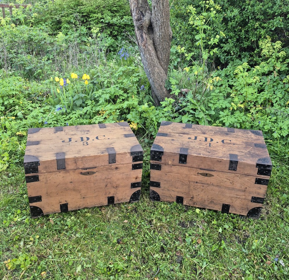 A pair of rectangular natural pine chests featuring black iron corner brackets, metal straps, keyhole escutcheons, and black stencilled text on the lids. View XI