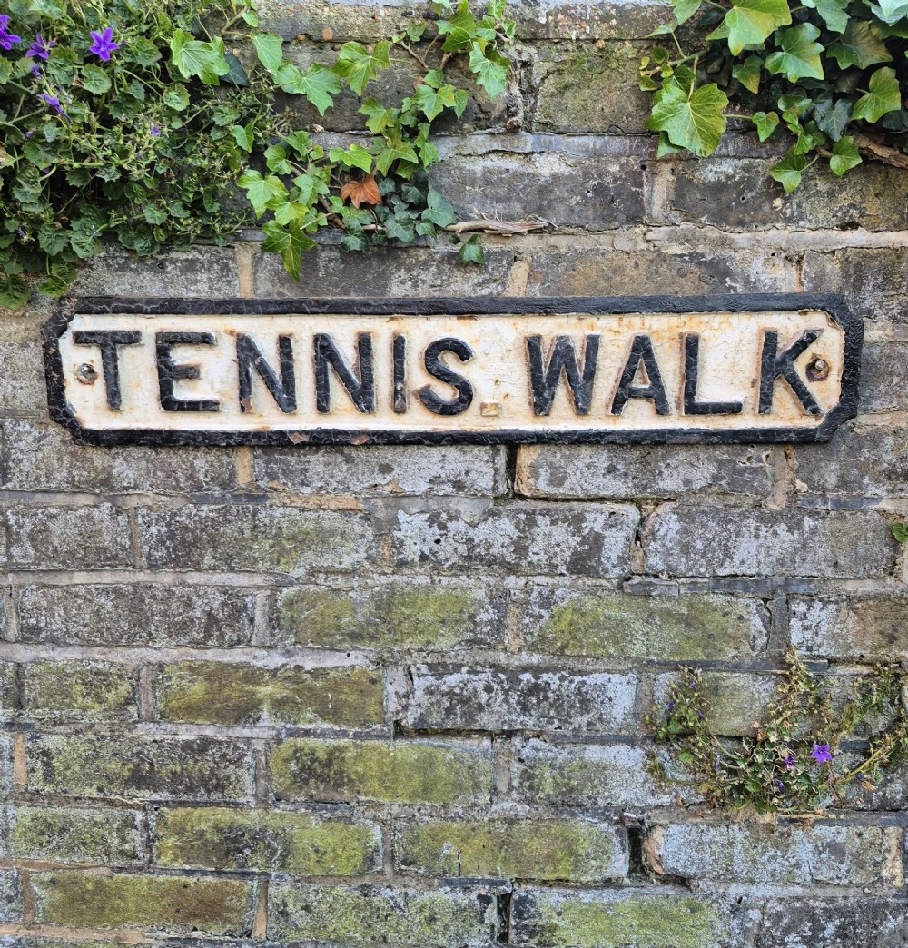 A rectangular 1920s cast iron street sign featuring embossed black lettering spelling TENNIS WALK on a weathered off-white background with a black border.