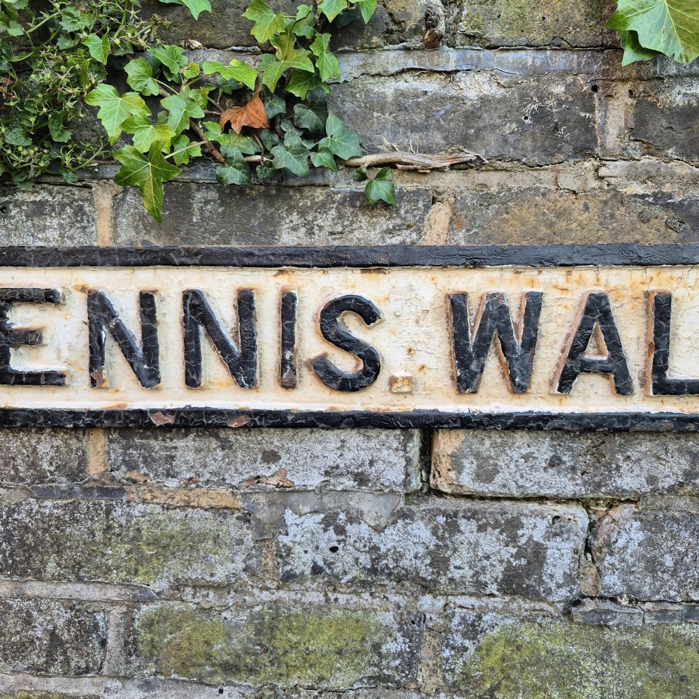 A rectangular 1920s cast iron street sign featuring embossed black lettering spelling TENNIS WALK on a weathered off-white background with a black border. View V
