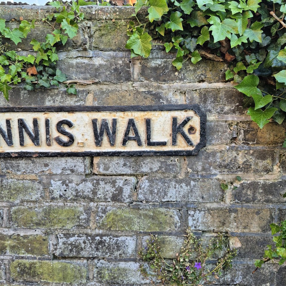 A rectangular 1920s cast iron street sign featuring embossed black lettering spelling TENNIS WALK on a weathered off-white background with a black border. View VI