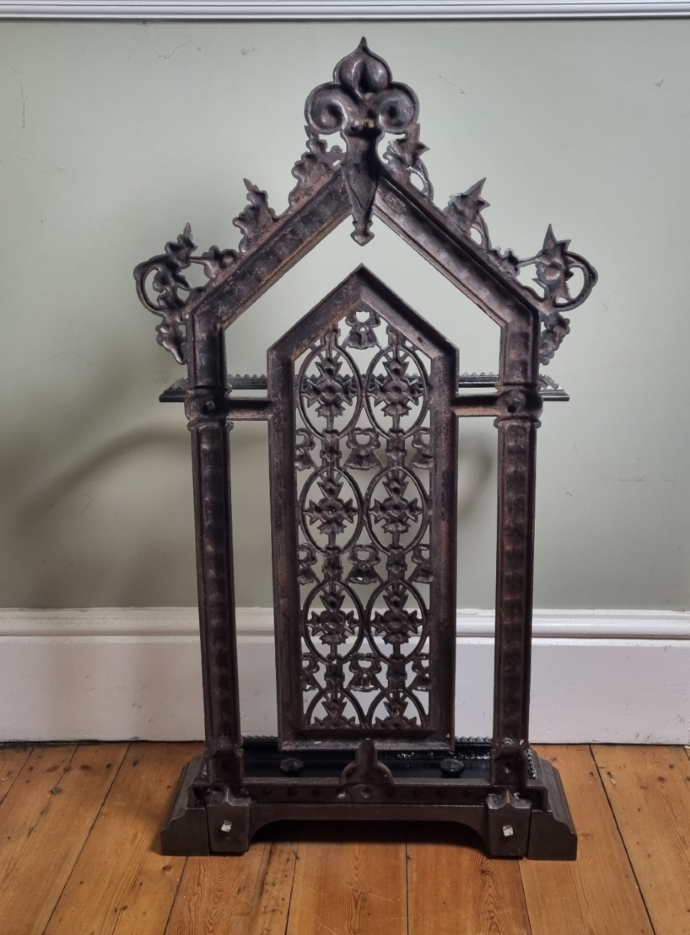 A Victorian cast iron stick stand featuring a pierced Gothic arch design, retention bar, and a rectangular drip tray base. View VII