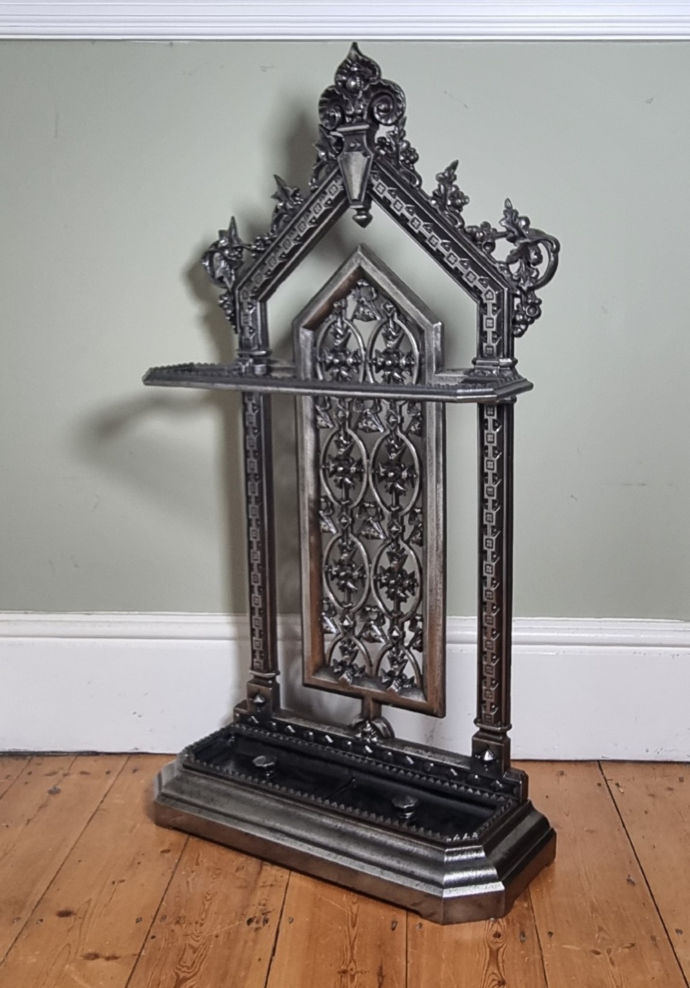 A Victorian cast iron stick stand featuring a pierced Gothic arch design, retention bar, and a rectangular drip tray base.