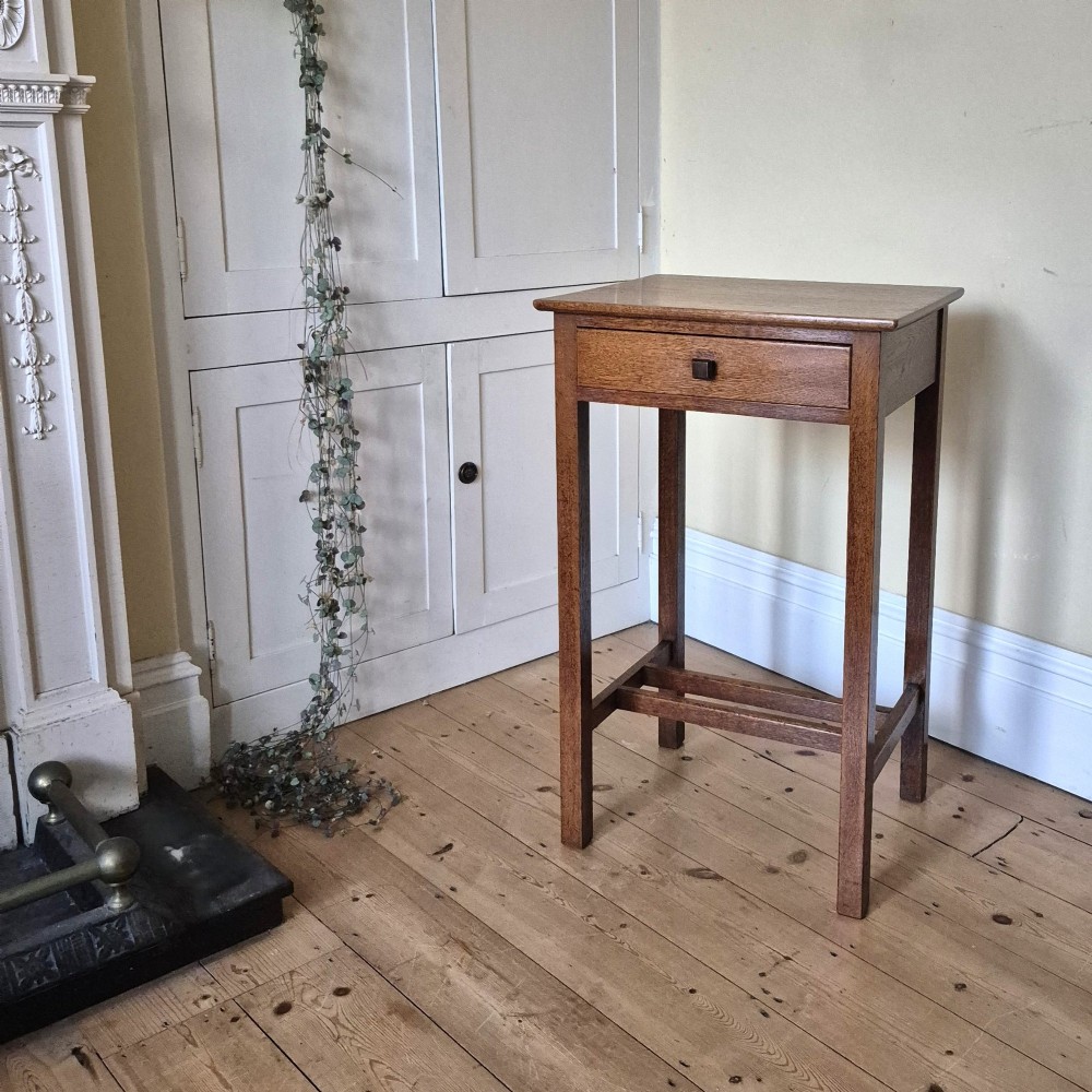 A tall rectangular oak side table featuring a single drawer with a square wooden knob and straight legs connected by a lower stretcher base. View III