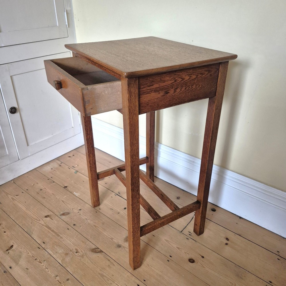 A tall rectangular oak side table featuring a single drawer with a square wooden knob and straight legs connected by a lower stretcher base. View V
