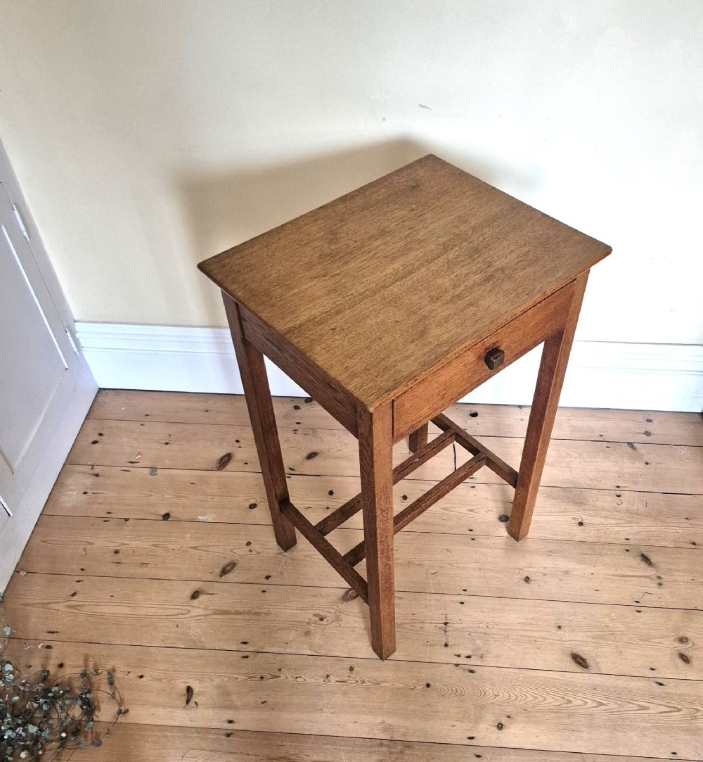 A tall rectangular oak side table featuring a single drawer with a square wooden knob and straight legs connected by a lower stretcher base. View VI