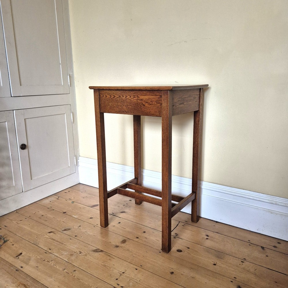 A tall rectangular oak side table featuring a single drawer with a square wooden knob and straight legs connected by a lower stretcher base. View VII