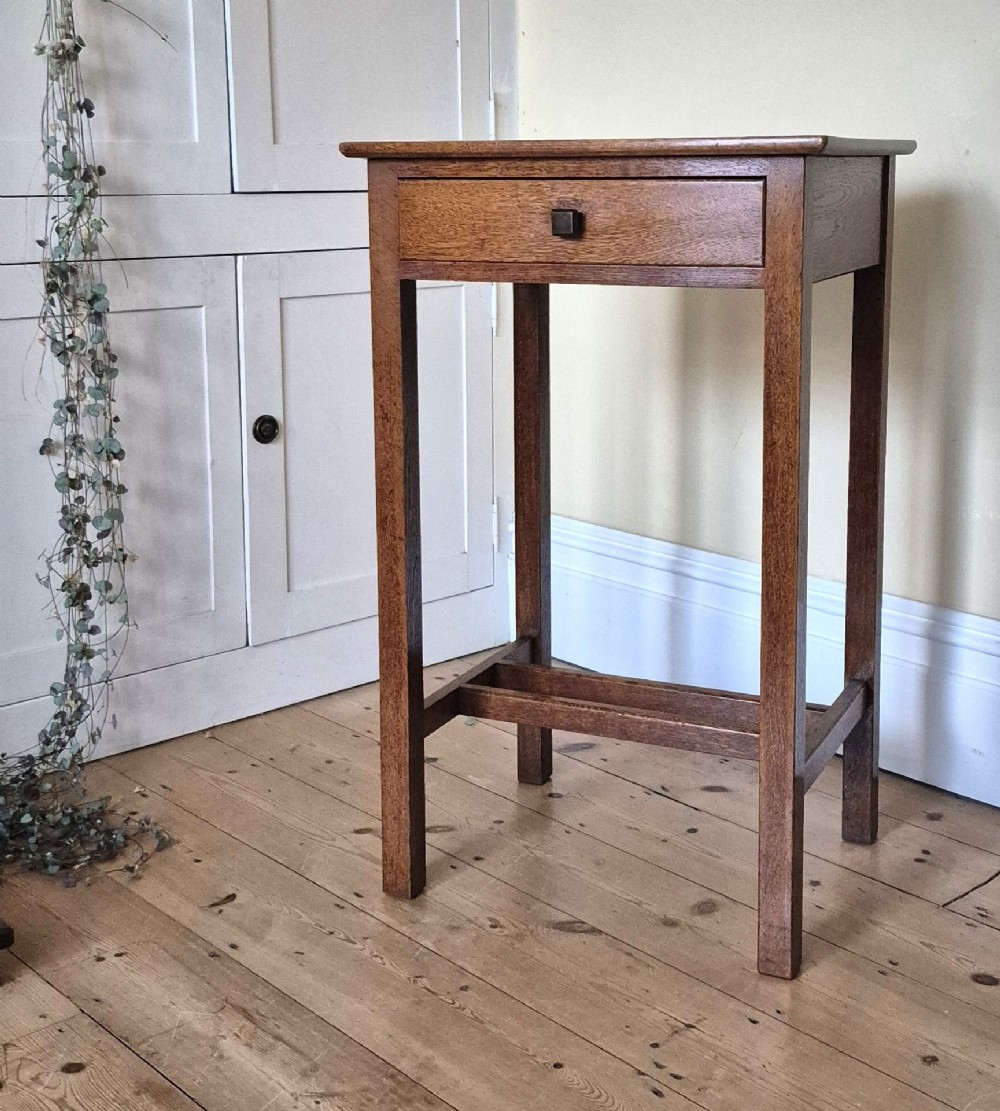 A tall rectangular oak side table featuring a single drawer with a square wooden knob and straight legs connected by a lower stretcher base.
